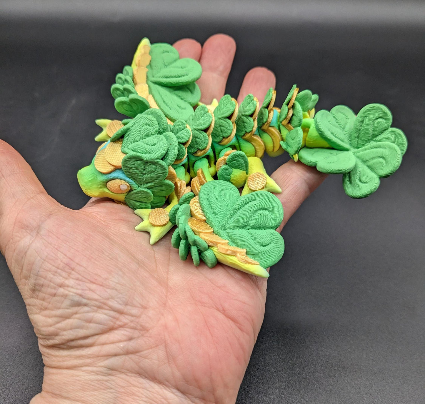 Meet our Adorable Tiny Baby Clover Dragon featuring intricate details & whimsical design, inspired by the luck & charm of clovers. Perfect for dragon enthusiasts or anyone who loves all things small. With the luck of the leprechaun, this little dragon is the perfect lucky charm. Small enough to carry in your pocket or display on desks, shelves, or computer.